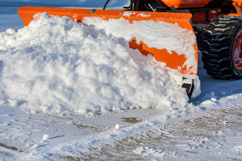 A bright orange snow plow pushes a large pile of snow out of the road.