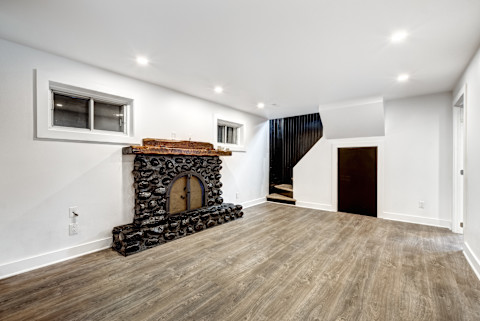 An elegant finished basement, complete with a living area with a rug and furniture. A staircase is visible on the right side of the image.