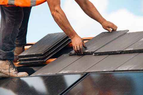 This image shows a roofing contractor laying roof tiles on a roof.