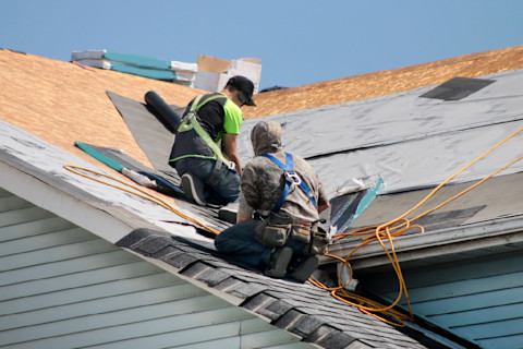 This image shows two professional roofers installing roof tiles on the roof of a residential property.