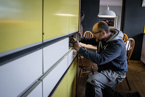 This image shows a handyman repairing a cabinet in a house.