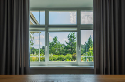 A calm outdoor view is seen through a window framed by curtains. Soft natural light creates a peaceful atmosphere.