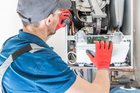 This image shows a HVAC worker wearing safety glasses and safety gloves fitting a furnace.