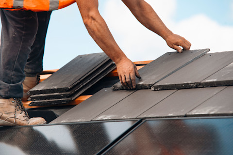 This image shows a roofing contractor laying roof tiles on a roof.