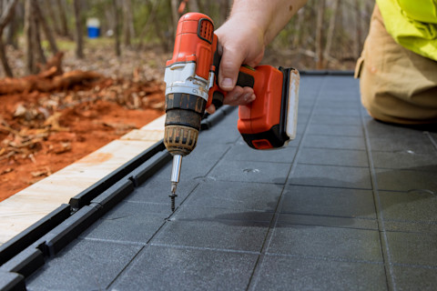 Closeup of a worker’s hand using a power drill to install a plastic or vinyl base for a garden shed.