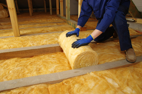 A worker rolls out mineral glass thermal insulation in an attic.